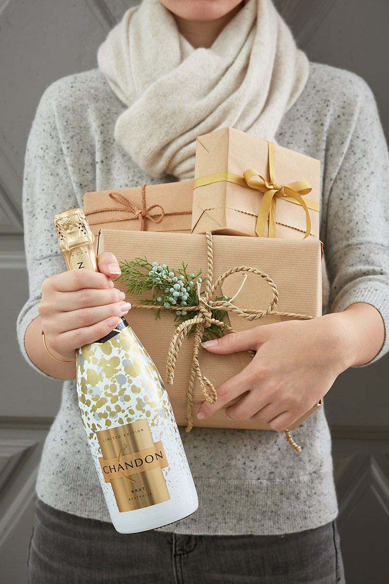 Jeune femme, les bras chargés de paquets cadeau, bouteille de Chandon à la main