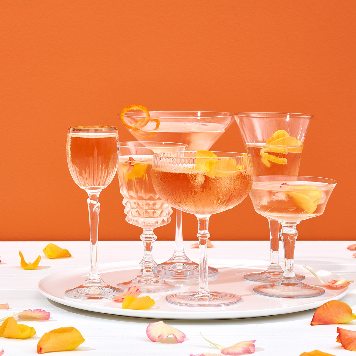 Verres et coupes de Champagne cocktail, pétales de roses fleurs,fond orange (Client Chandon 2019)