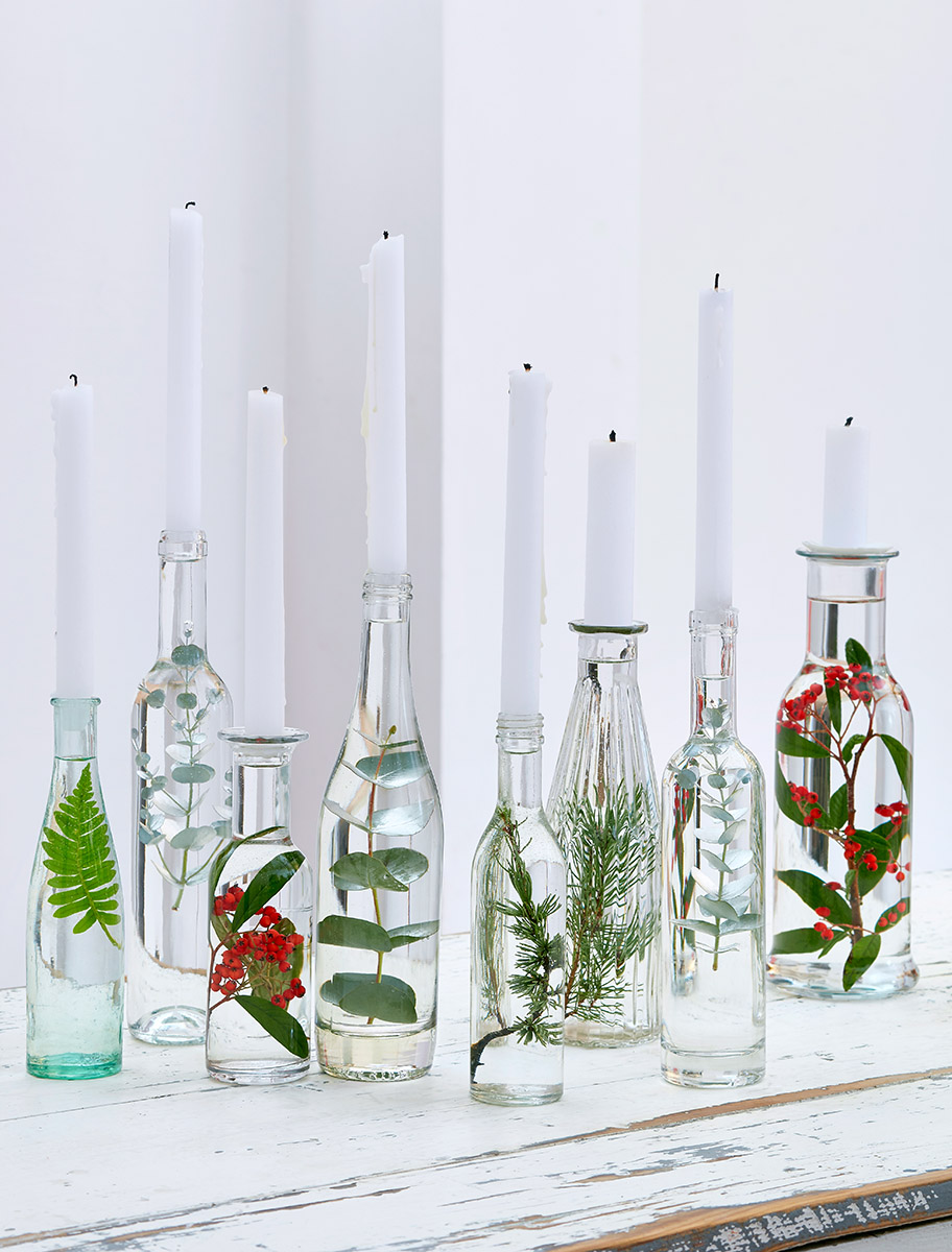 Nature morte : collection de bouteilles bougeoirs contenant des feuilles, décoration de Noël