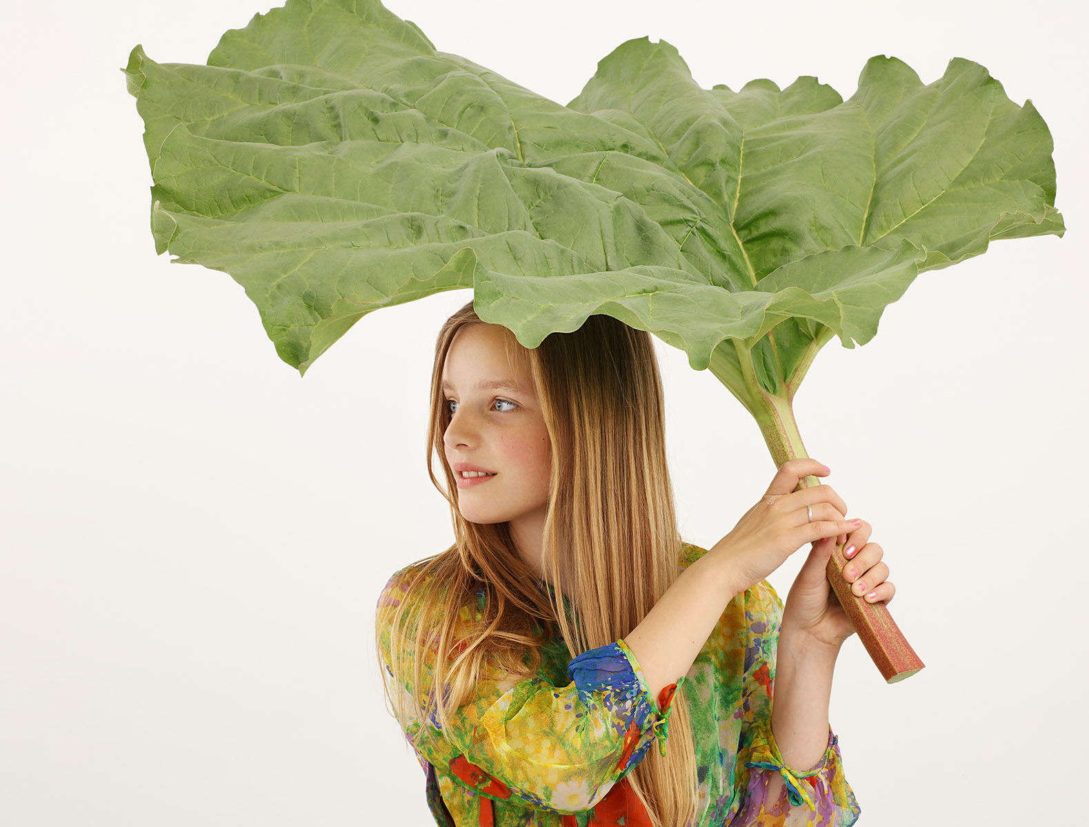 Portrait jeune fille tenant une grande feuille de rhubarbe au dessus d'elle