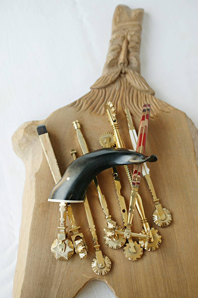 Roulettes de patisserie Sardes posées sur une planche à découper avec un visage d'homme sculpté sue le manche